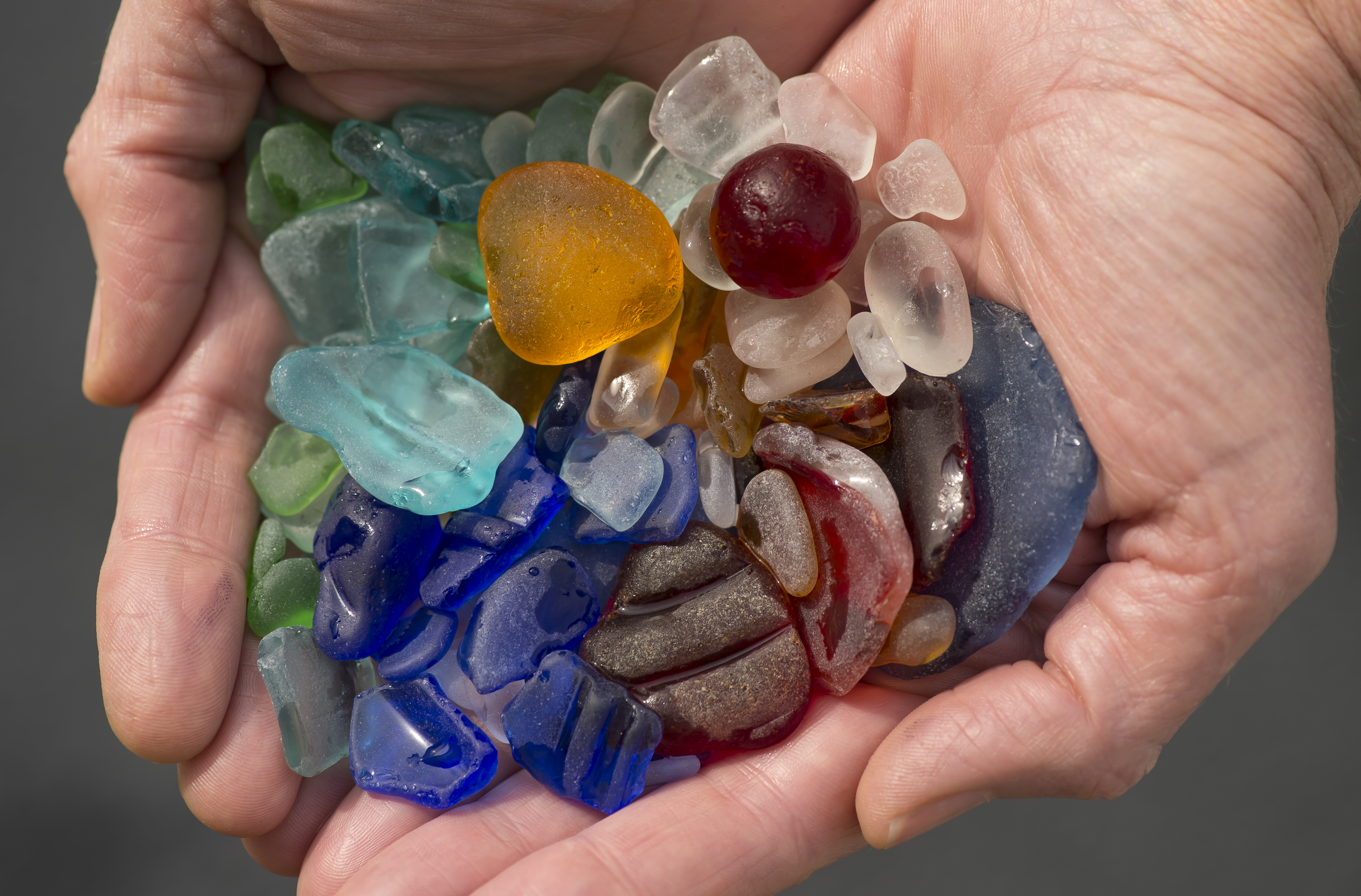 A close-up shot of two hands holding about two dozen small pieces of beach glass. A close-up shot of two hands holding about two dozen small pieces of beach glass.
